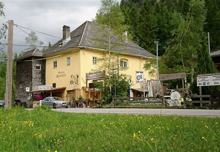 A yellow building with a rustic façade stands at the street corner. Surrounded by green grass and trees, it conveys an inviting atmosphere.