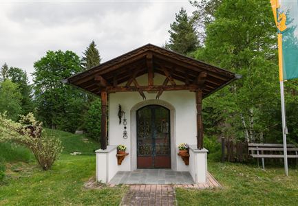 Ein kleines, charmantes Gebäude mit einem Holzüberdach und einer Eingangstür. Umgeben von grünen Bäumen und einer gepflegten Gartenanlage.