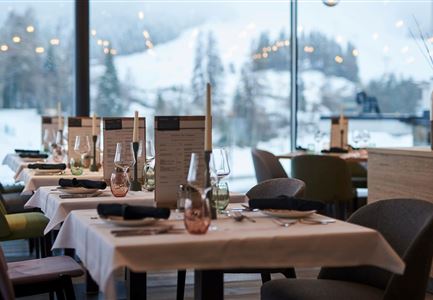 Ein elegantes Restaurant mit schön gedeckten Tischen und großen Fenstern. Im Hintergrund ist eine schneebedeckte Landschaft sichtbar.