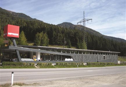 Ein modernes Geschäft mit einer großen roten Werbung und einer eleganten Fassade. Im Hintergrund sind Bäume und Berge zu sehen.