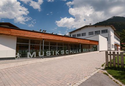 A modern music school with large windows and an inviting entrance area. In the background, there are mountains and a blue sky.