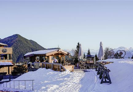 A cozy alpine hut in a snowy mountain landscape. In the background, snow-covered mountains and a clear sky can be seen.