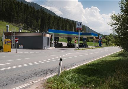 A gas station on a country road surrounded by trees and mountains. The sky is partly cloudy.