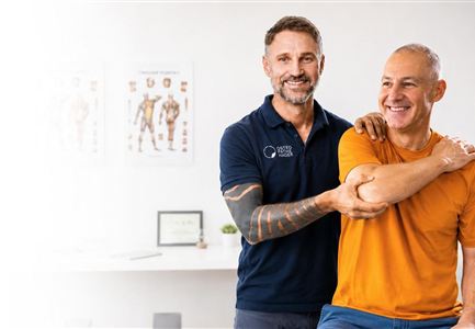 Ein Physiotherapeut hilft einem Patienten bei einer Übung. Beide Personen lächeln und zeigen eine positive Interaktion.