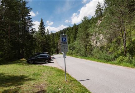 Ein Aussichtspunkt in der Natur mit einer Parkuhr und parkenden Autos. Umgeben von Bäumen und einem klaren Himmel.