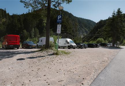 Ein Parkplatz in der Natur mit mehreren Autos. Im Hintergrund sind Wälder und Berge zu sehen.