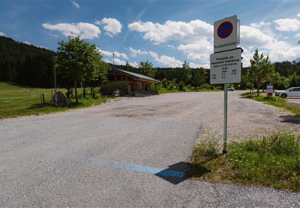 Ein Parkplatz in ländlicher Umgebung mit einer klaren blauen Himmel. Im Hintergrund befindet sich ein kleines Gebäude und einige Bäume.