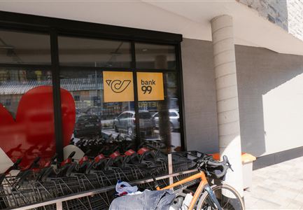 Ein Fenster mit dem Logo der Bank 99 und einem großen roten Herz. Im Vordergrund stehen Einkaufswagen und ein Fahrrad.