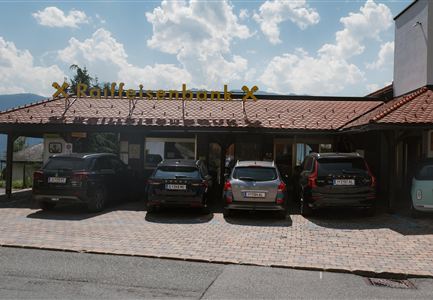 A restaurant with an inviting entrance and several cars in the parking lot. The sky is blue with some clouds.