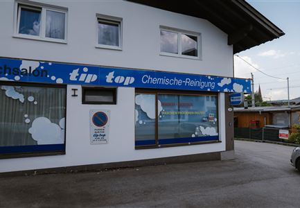 A business for dry cleaning with the sign "tip top". The facade is in white and blue, with some windows and a parked car in front.