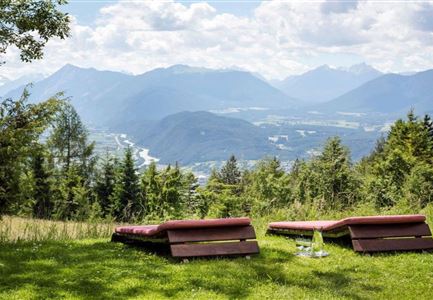 Eine entspannende Aussicht auf die Berge mit Liegen auf der grünen Wiese. Im Hintergrund fließt ein Fluss durch das Tal.