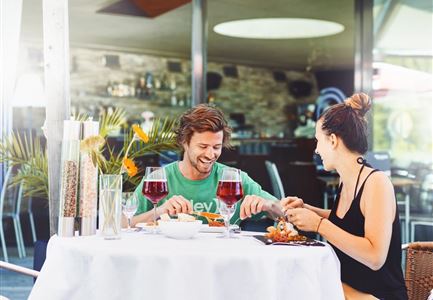 Ein fröhliches Paar genießt ein Abendessen in einem eleganten Restaurant. Auf dem Tisch stehen zwei große Weingläser und eine Auswahl an köstlichen Speisen.