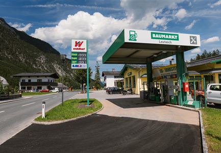 A gas station with a market in a rural setting. In the background, mountains and a street view can be seen.