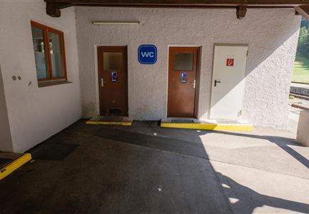 A space with two toilet doors, one for men and one for women. The walls are white and it is sunny.