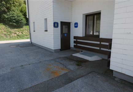 An outdoor toilet with access through a wooden cladding. The building is bright and modern, surrounded by a green landscape.
