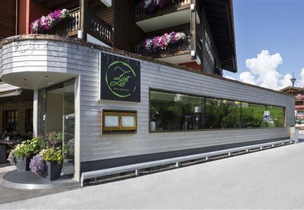 Ein modernes Restaurant mit einer großen Fensterfront. Blumenpflanzen dekorieren den Eingang und schaffen eine einladende Atmosphäre.