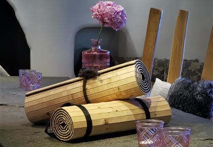 Zwei schöne Holzrollen liegen auf einem Tisch. Im Hintergrund steht eine Vase mit pinken Blumen und einige gläserne Kerzenhalter.
