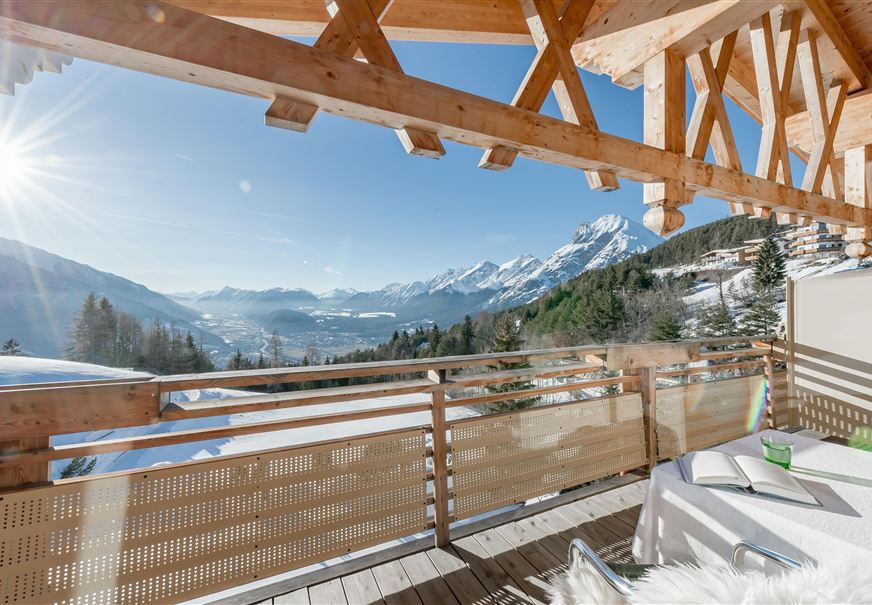 Een prachtig uitzicht vanaf een balkon terras op besneeuwde bergen. De zon straalt en de lucht is helder en blauw.