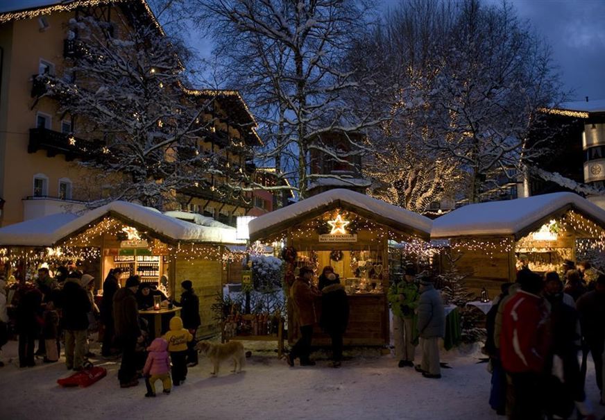 Un mercatino di Natale festivo con bancarelle illuminate sotto un cielo notturno chiaro. Le persone godono dell'atmosfera festosa nella neve.