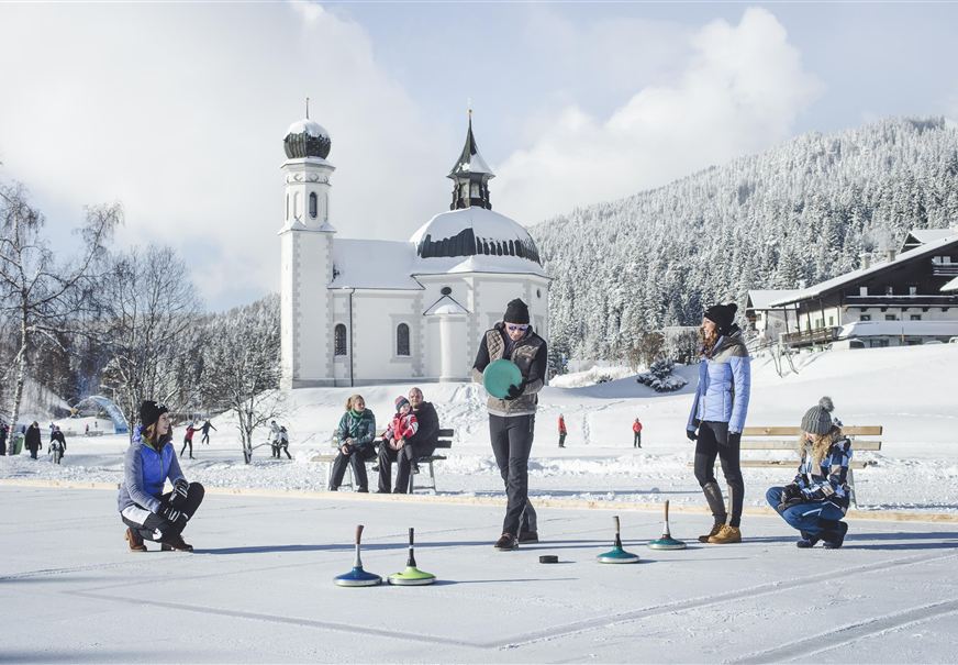 Een winterlandschap met een kerk op de achtergrond. Groepen mensen spelen op een bevroren oppervlak.