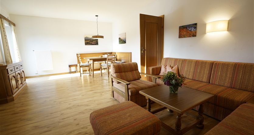A cozy living space with a sofa and a coffee table. In the background, there is a dining area with a table and chairs.