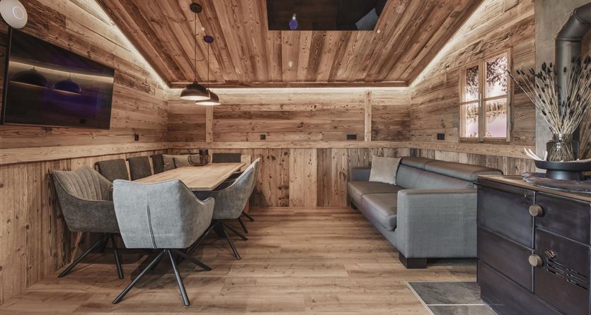 A cozy room with wooden-paneled walls and a modern table. Comfortable chairs and a couch create an inviting atmosphere.