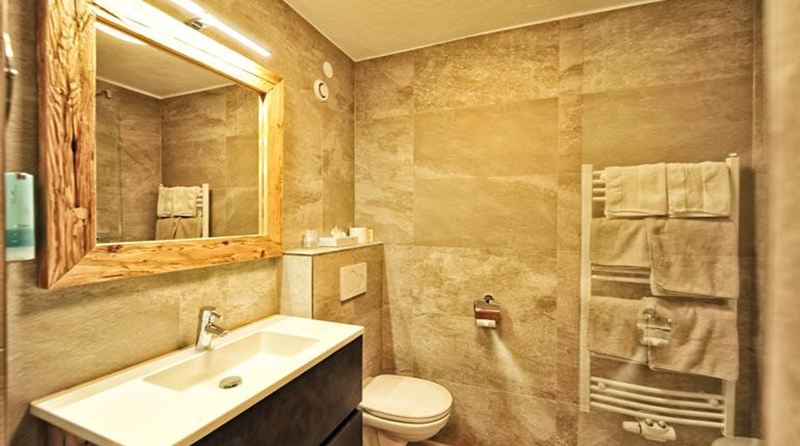 Un bagno moderno con colori caldi e neutri.  
Ci sono un lavandino, un WC e un scaldasalviette.
