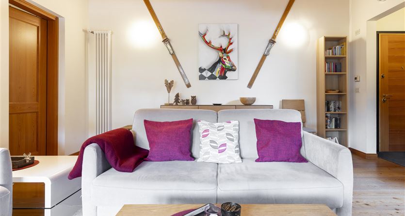 Ein modernes Wohnzimmer mit einem bequemen Sofa und dekorativen Kissen. An der Wand hängen Holzski und ein gemaltes Bild eines Rentiers.