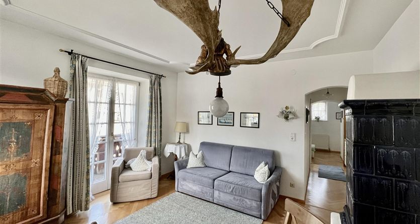 Un accogliente soggiorno con un grande lampadario a corna e mobili moderni. Le pareti sono chiare e ci sono grandi finestre che lasciano entrare molta luce.