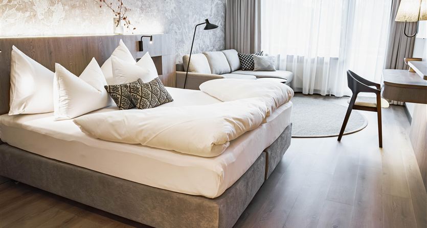 Una camera da letto moderna con un grande letto e diversi cuscini. Accanto c'è una poltrona comoda e un tavolo.