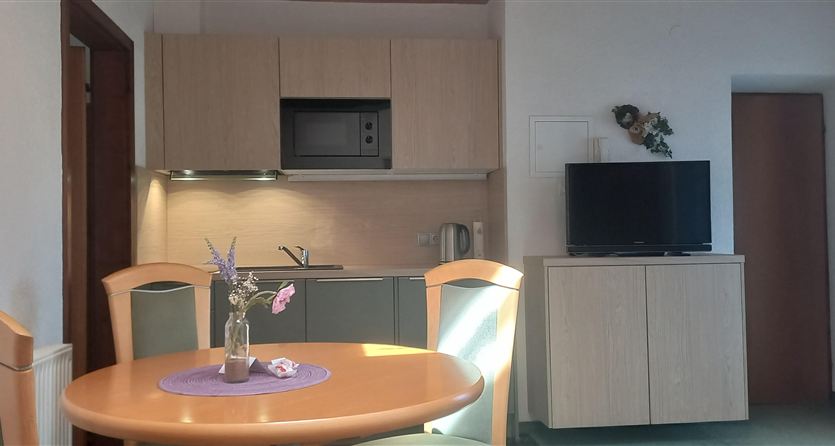 Una cucina moderna con un tavolo da pranzo rotondo e quattro sedie. La stanza è luminosa e accogliente, con una televisione e elementi decorativi.