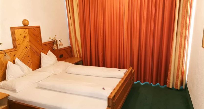 Ein gemütliches Zimmer mit einem Doppelbett und einem großen Fenster. Die Vorhänge sind orange, und der Teppich ist grün.