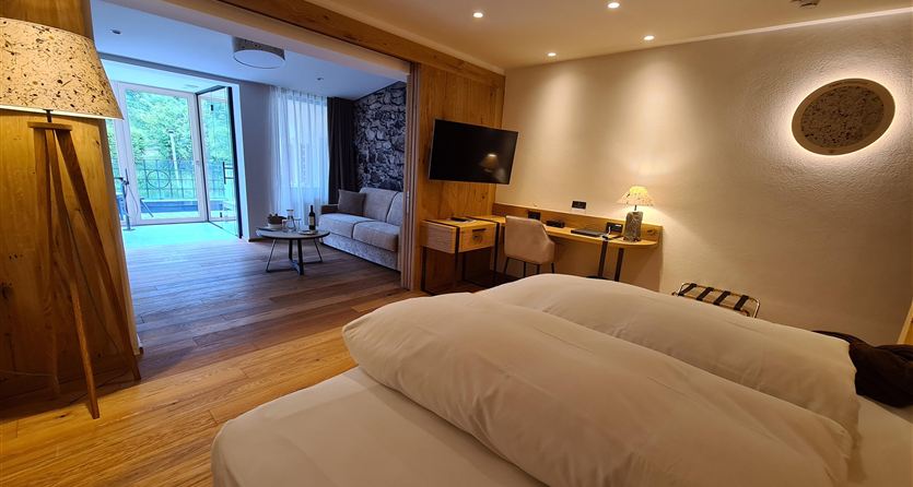 Una camera d'hotel elegante con un letto moderno e una scrivania.  
Sul fondo c'è un soggiorno accogliente con accesso al terrazzo.