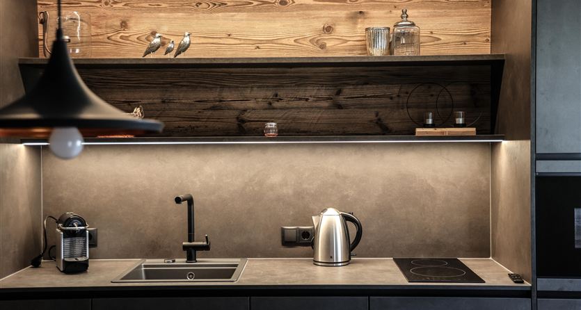 Een moderne keuken met eenvoudige, elegante meubels en houten planken. Op het aanrecht zijn een waterkoker en een koffiezetapparaat zichtbaar.