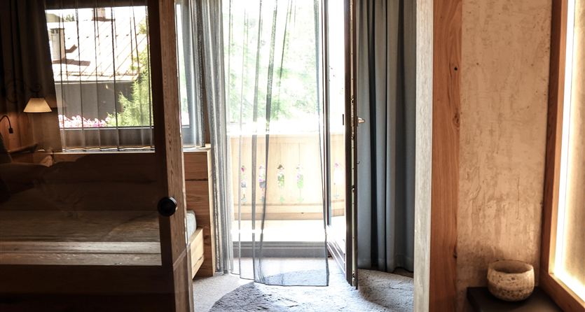 Una stanza accogliente con una cornice in legno e una finestra che conduce a un balcone. Il pavimento è fornito di un tappeto rotondo e un tappeto chiaro.