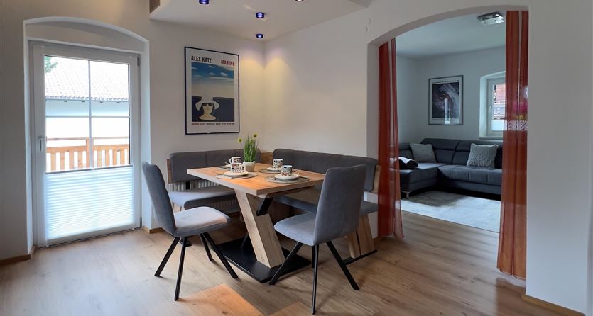 Een moderne eetkamer met een tafel en stoelen. Op de achtergrond is een gezellige woonkamer te zien.