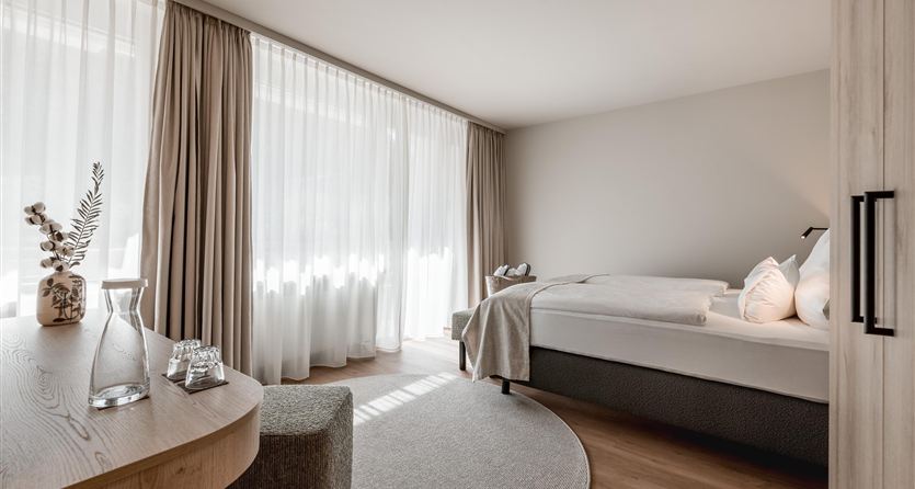 A modern bedroom with large windows and plenty of light. The room is simply and elegantly furnished with a bed and a round carpet.