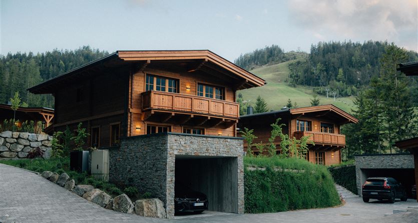 Zwei moderne Chalets aus Holz in einer ruhigen Landschaft. Die Umgebung ist grün mit sanften Hügeln im Hintergrund.