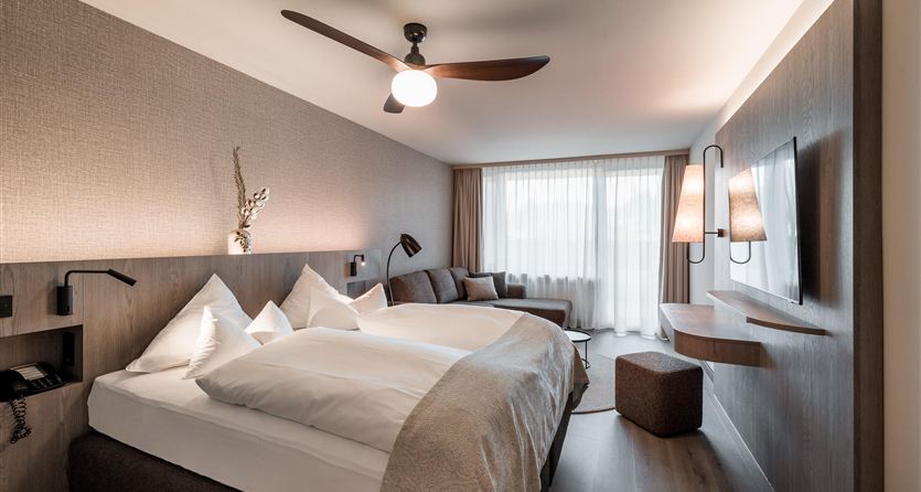 A modern hotel room with two beds and a large window. The decor is simple and elegant with soft colors.