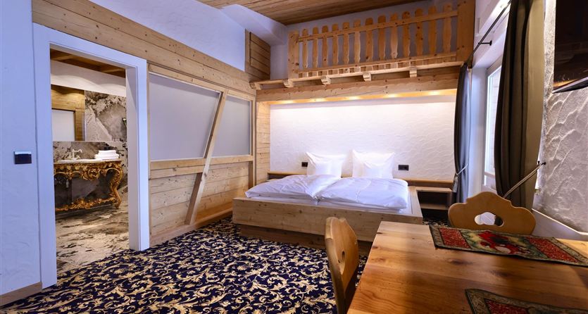 Ein gemütliches Zimmer mit einem Doppelbett, Holzdetails und einem rustikalen Teppich. Es gibt einen Tisch und Stühle, die eine einladende Atmosphäre schaffen.