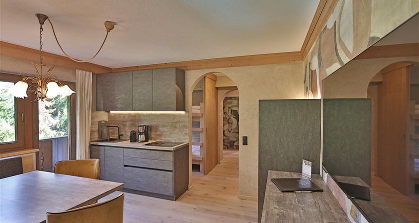 Eine moderne Küchenzeile mit Holzregalen und einem Essbereich. Der Raum ist hell und freundlich, mit großen Fenstern und zeitgemäßem Design.