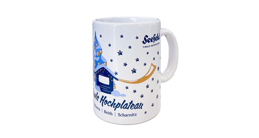 Eine weiße Tasse mit blauem Druck. Der Aufdruck zeigt einen fantasievollen Entwurf mit einem kleinen Haus und einem Charakter in Weihnachtskleidung.