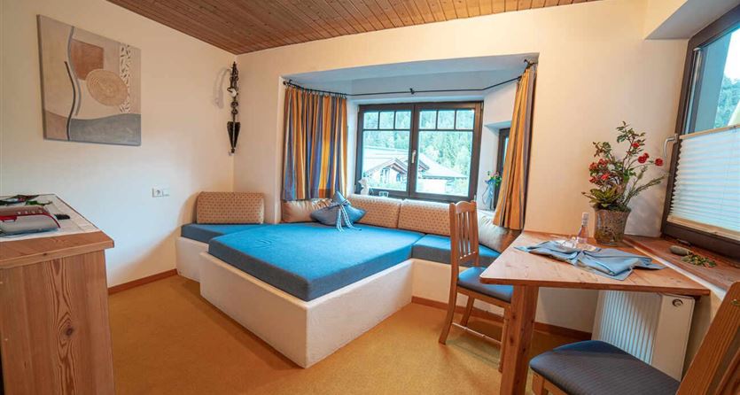 Een gezellige kamer met een blauwe slaapruimte en een eettafel. Grote ramen bieden uitzicht op het landschap.