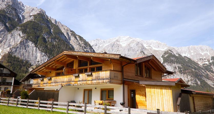A beautiful traditional wooden house in the mountains. The impressive peaks and the green grass frame the landscape.