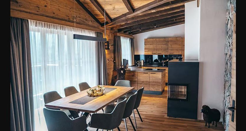Een moderne, lichte eetkamer met een grote houten tafel en elegante stoelen. De open ramen zorgen voor veel daglicht en een gezellige sfeer.