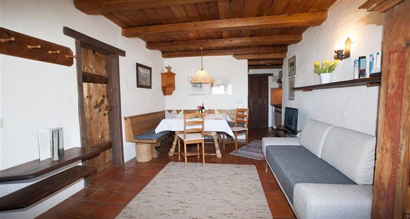 Een gezellige woonkamer met een houten plafond en warme kleurtonen. Er is een eetgedeelte met een tafel en stoelen, evenals een comfortabel grijs bank.