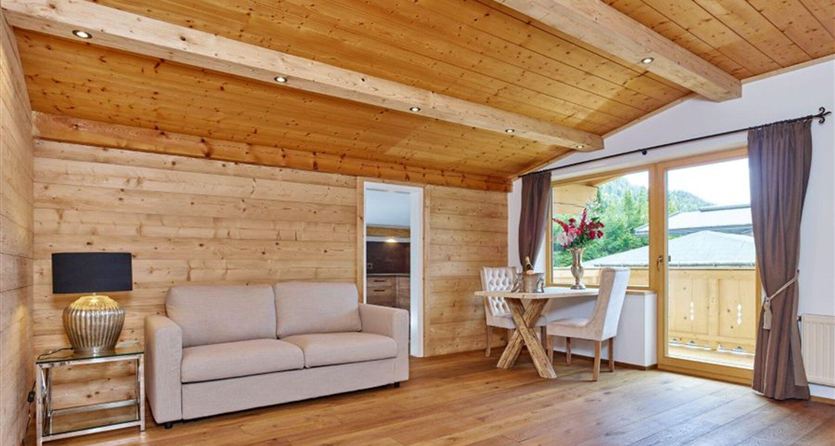 Een gezellige woonkamer met houtbekleding en een groot raam. Een bank en een tafel met stoelen nodigen uit tot ontspannen.