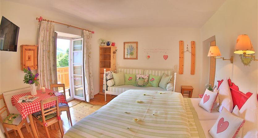 A cozy room with a large bed and a small table. The windows provide plenty of light and offer a view outside.