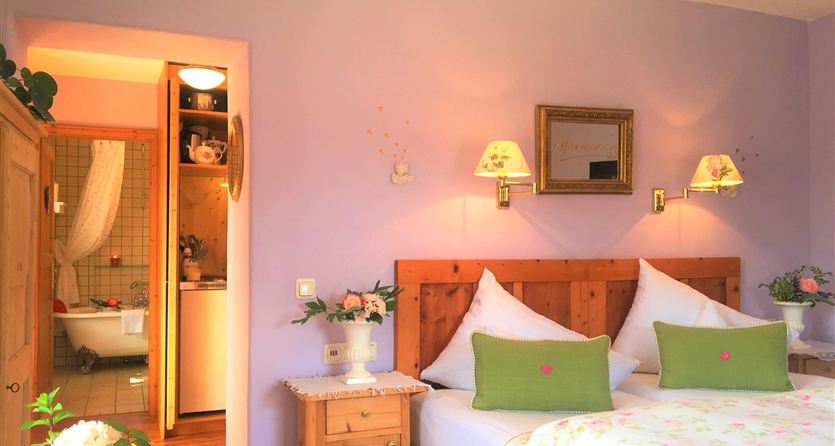 Een gezellige slaapkamer met paarse muren en twee bedden. Op de achtergrond is een badkamer zichtbaar, en bloemen zorgen voor een vriendelijke sfeer.