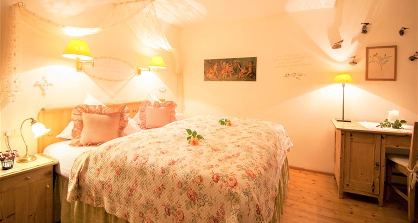 A cozy bedroom with a large bed and floral bedding. The soft lighting creates a relaxed atmosphere.